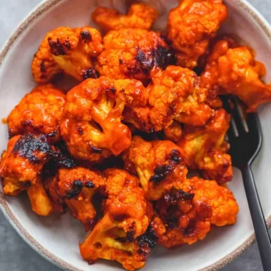 Bowl of Easy Buffalo Cauliflower with spicy sauce and garnishes