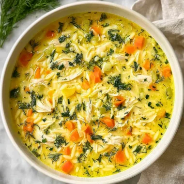 Bowl of Greek Lemon Chicken Soup with lemon slices and herbs on a wooden table
