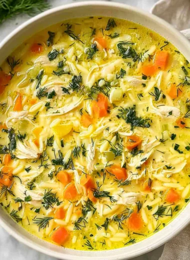 Bowl of Greek Lemon Chicken Soup with lemon slices and herbs on a wooden table