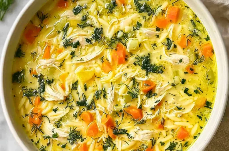 Bowl of Greek Lemon Chicken Soup with lemon slices and herbs on a wooden table