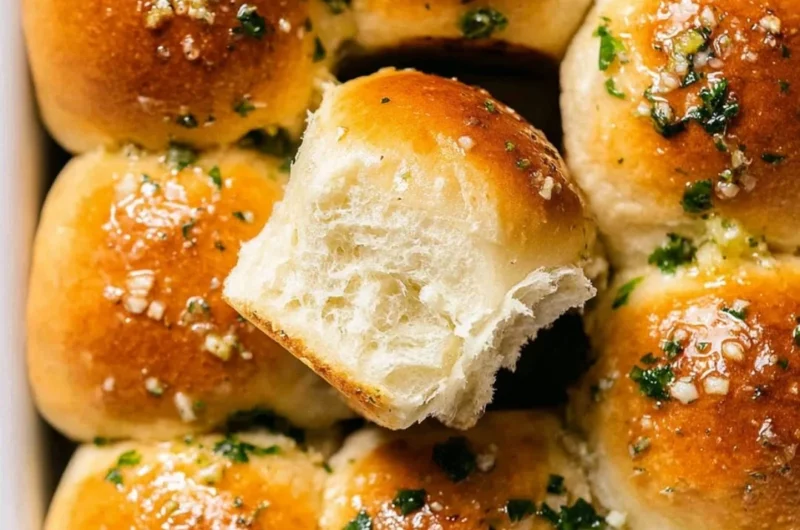Homemade garlic bread rolls served on a wooden platter with butter.