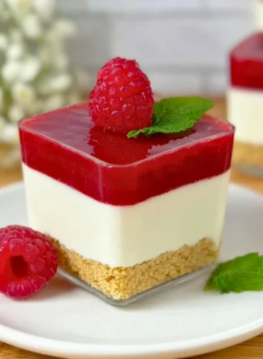 Layered Raspberry Cheesecake in a glass with fresh raspberries and cream
